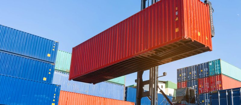 Forklift raising container in port cargo yard.